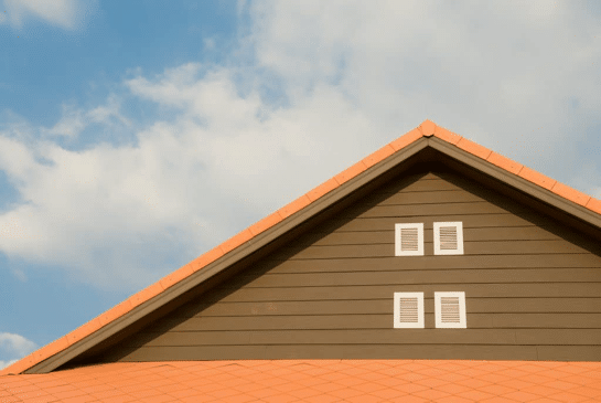 The gable of a house with a terracotta shingle roof against a blue sky with white clouds