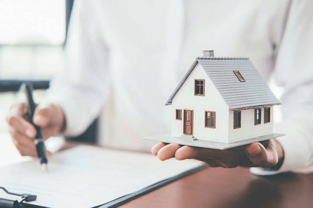An attorney holding a small model house while reviewing an insurance policy
