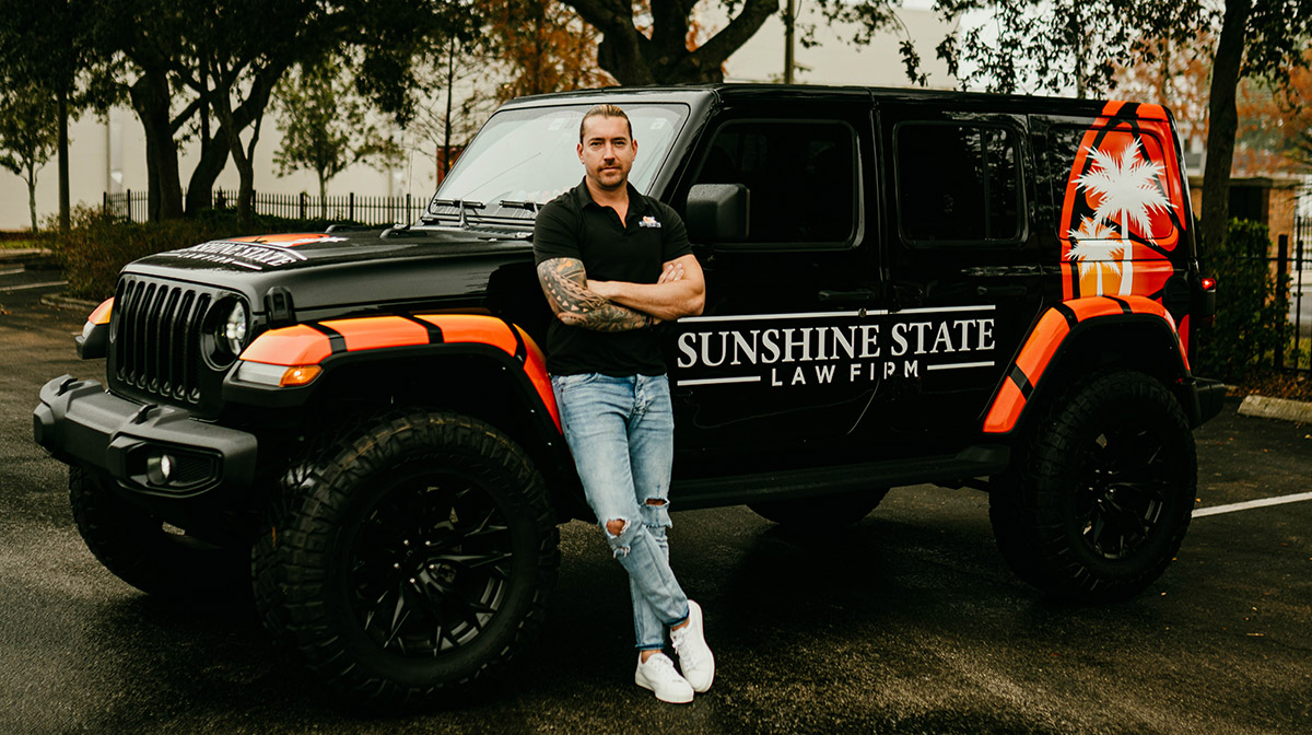 A Sunshine State Law Firm team member standing beside the black Sunshine State Law Firm Jeep